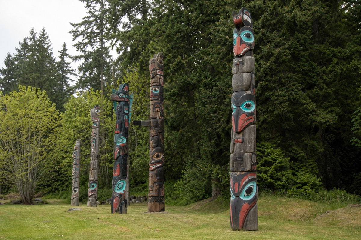 A row of carved cedar totem poles standing in a green public park on Vancouver Island under soft daylight